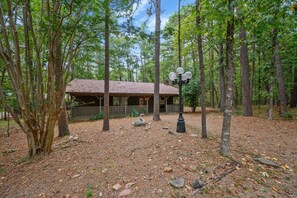 A rustic cabin with a thatched roof, surrounded by a forested area with a dirt ground.