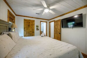 A bedroom with a large bed, wooden doors, a ceiling fan, and a flat-screen TV. - EZ Ridge Retreat | Rustic Broken Bow Lake Cabin with Hot Tub, Fire Pit, Grill & Pets (Hochatown)