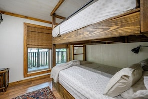 A bunk bed room with a window, a wooden floor, and a small table.