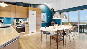 A modern kitchen with wooden cabinets, a white refrigerator, and a dining area with a round table and chairs. - "Berta" - 70m to the fjord by Interhome (Roslev)