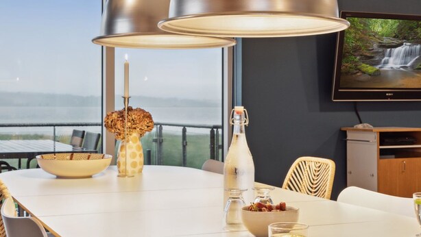 A dining area with a table set for two, a television mounted on the wall, and a view of a waterfall through large windows. - "Berta" - 70m to the fjord by Interhome (Roslev)