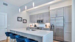 Una cocina moderna con una isla central, taburetes de bar, electrodomésticos de acero inoxidable y armarios color gris claro.