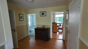 A hallway with wooden flooring, a dark wooden cabinet, and a door leading to a room with a window.