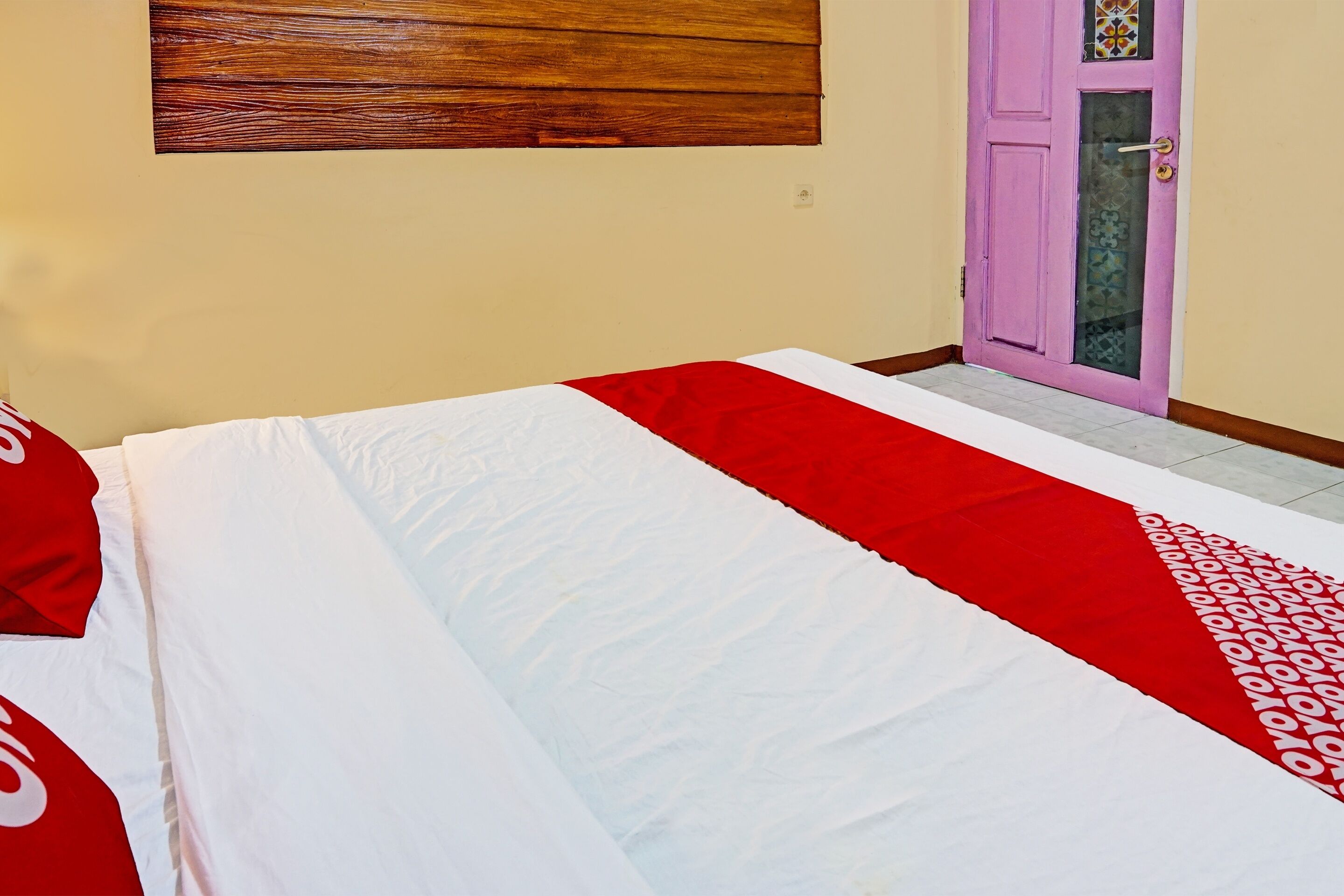 Una cama con una colcha blanca y roja, un cabecero de madera y una puerta rosa con una ventana.