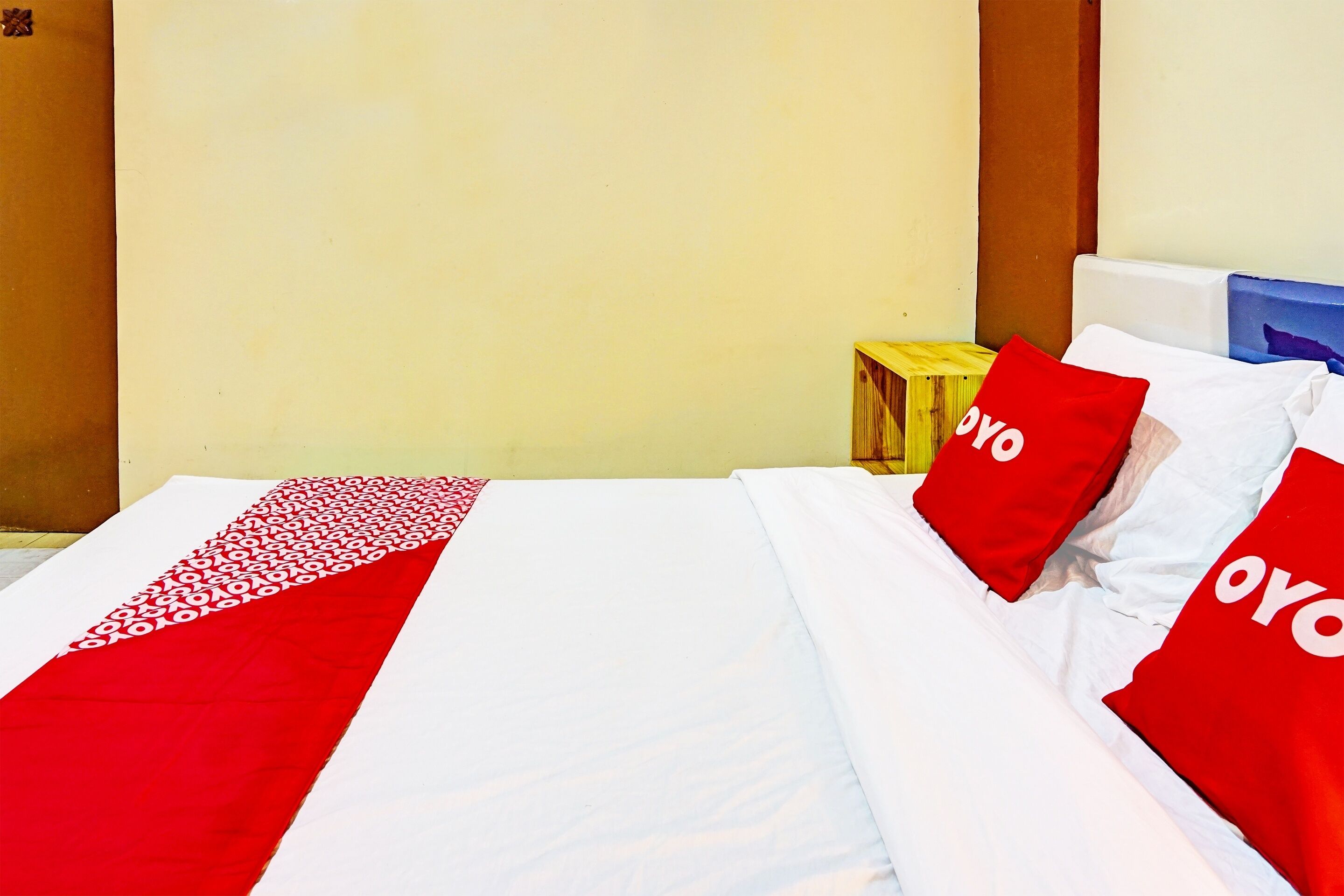 Een hotelkamer met een bed, voorzien van rode en witte beddengoed, een houten hoofdeinde en een nachtkastje met een lamp.