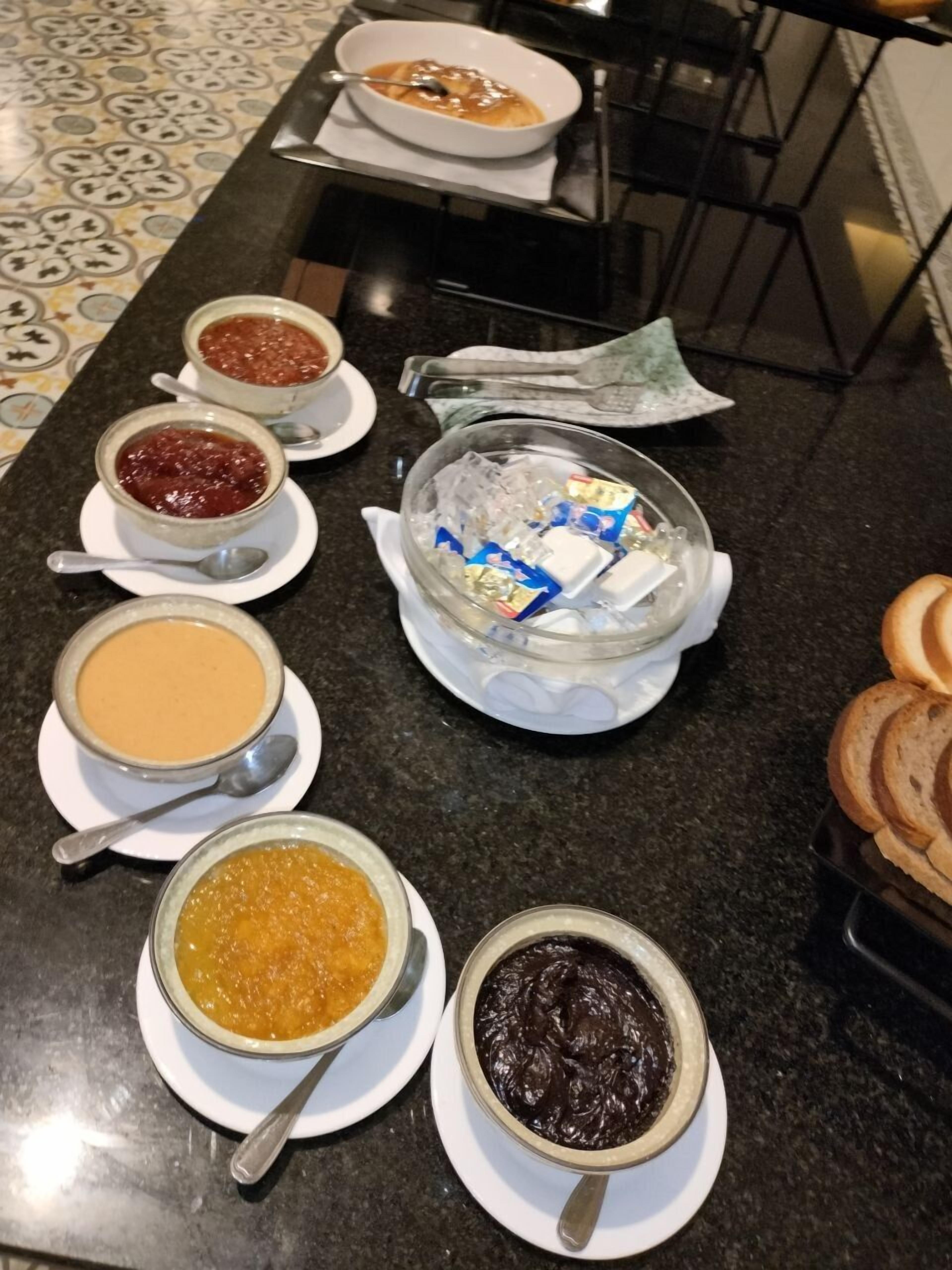 A table with various bowls of food, including soups and spreads, and a glass bowl with ice and condiments.