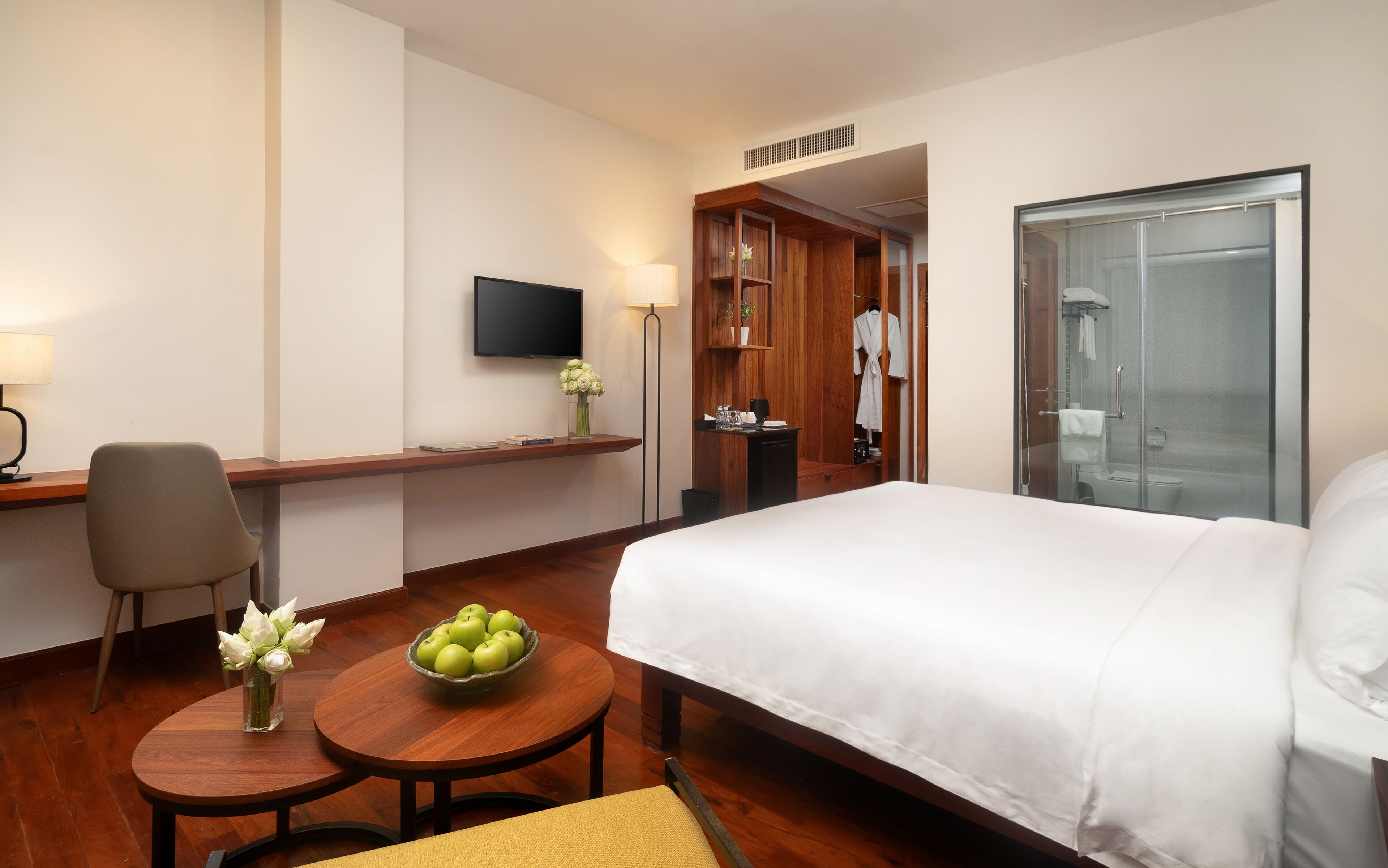 Ein Hotelzimmer mit einem Bett, einem Schreibtisch mit Stuhl, einem kleinen Tisch mit einer Schüssel Äpfeln, einem Fernseher an der Wand und einem Duschbereich.