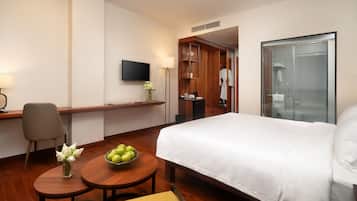 Ein Hotelzimmer mit einem Bett, einem Schreibtisch mit Stuhl, einem kleinen Tisch mit einer Schüssel Äpfeln, einem Fernseher an der Wand und einem Duschbereich.