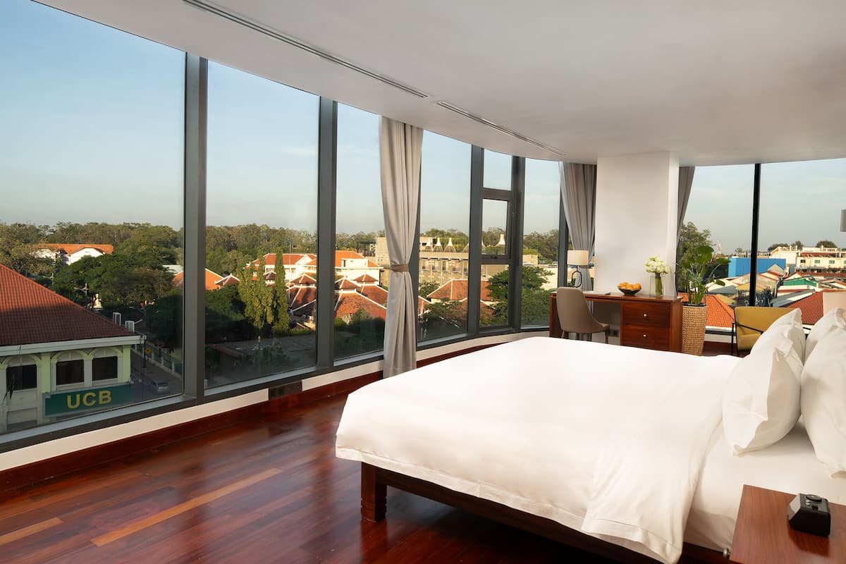 Een hotelkamer met een groot bed, een bureau met stoel en uitzicht op de stad door grote ramen.