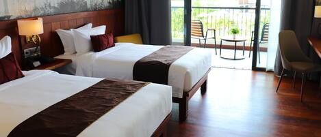 A hotel room with two beds, a balcony with a table and chairs, and a desk with a chair.