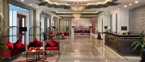 A spacious lobby with a reflective marble floor, red upholstered seating, a reception desk, and a large chandelier.