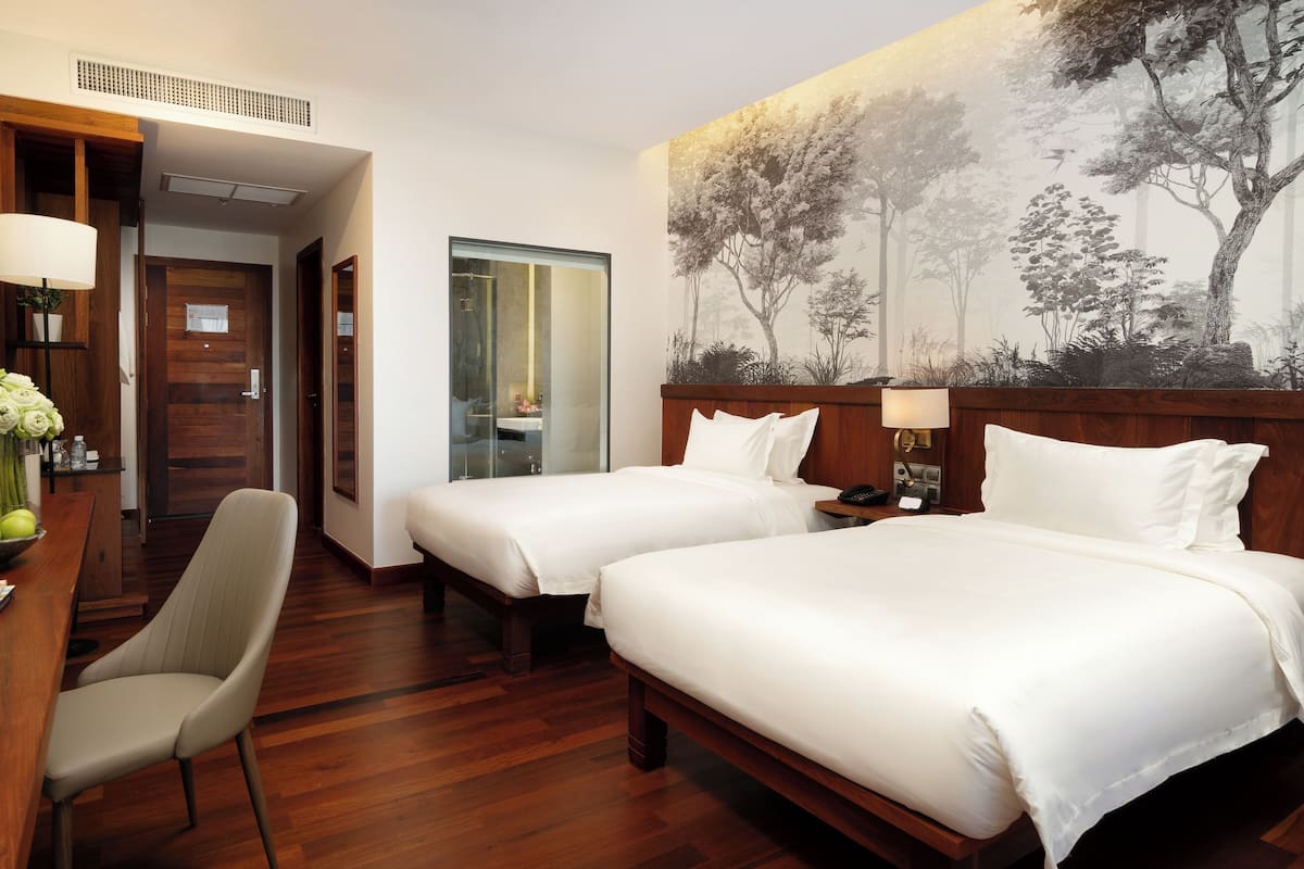Een hotelkamer met twee bedden, een bureau met een stoel, een bloemenvaas en een groot wanddecor.