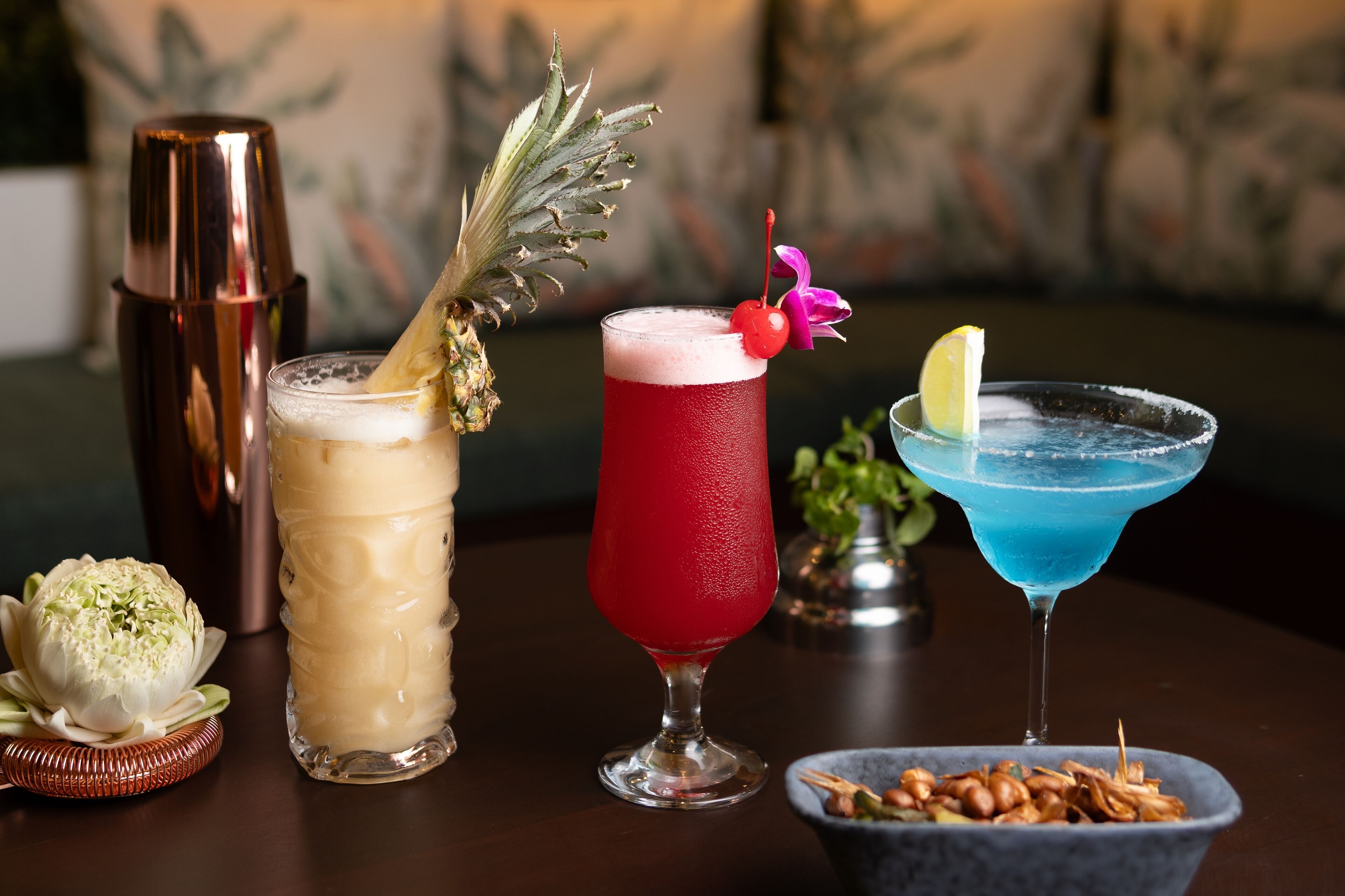 Trois cocktails sont posés sur une table, accompagnés d’un shaker à cocktails et d’un bol de noix.