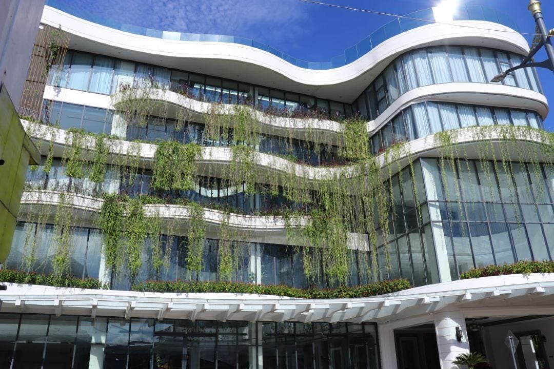 Un bâtiment moderne à l’architecture aux lignes courbes, doté de grandes fenêtres et de plantes vertes sur les balcons.