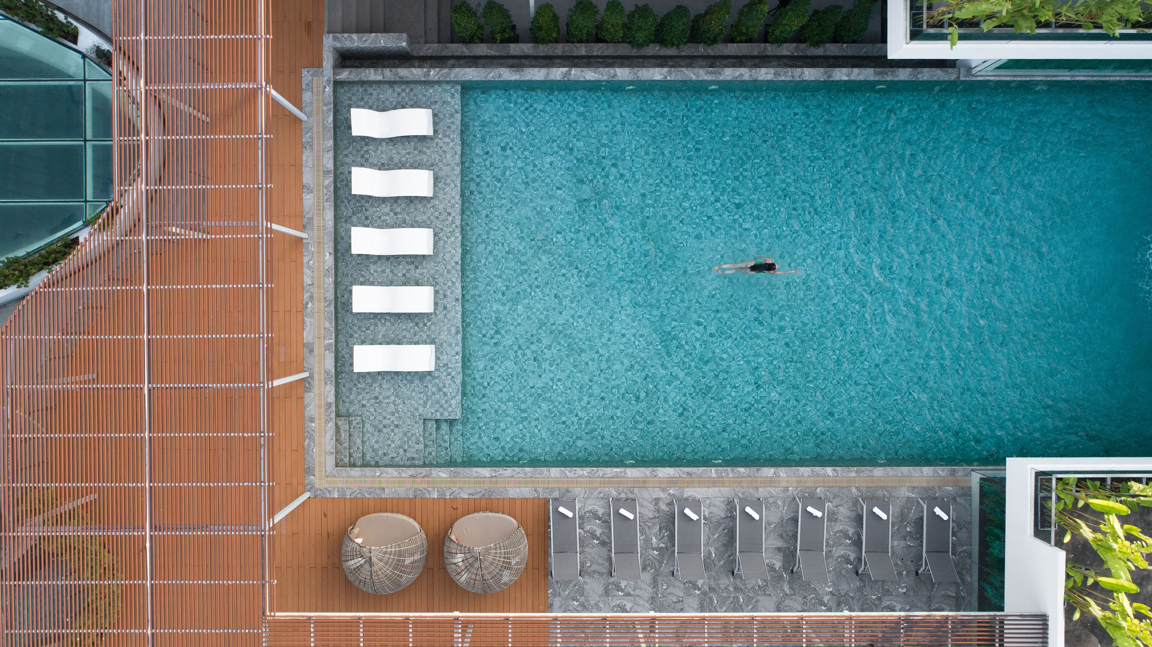 Vista aèria d'una piscina amb una persona nedant, envoltada de gandules i tumbonas.