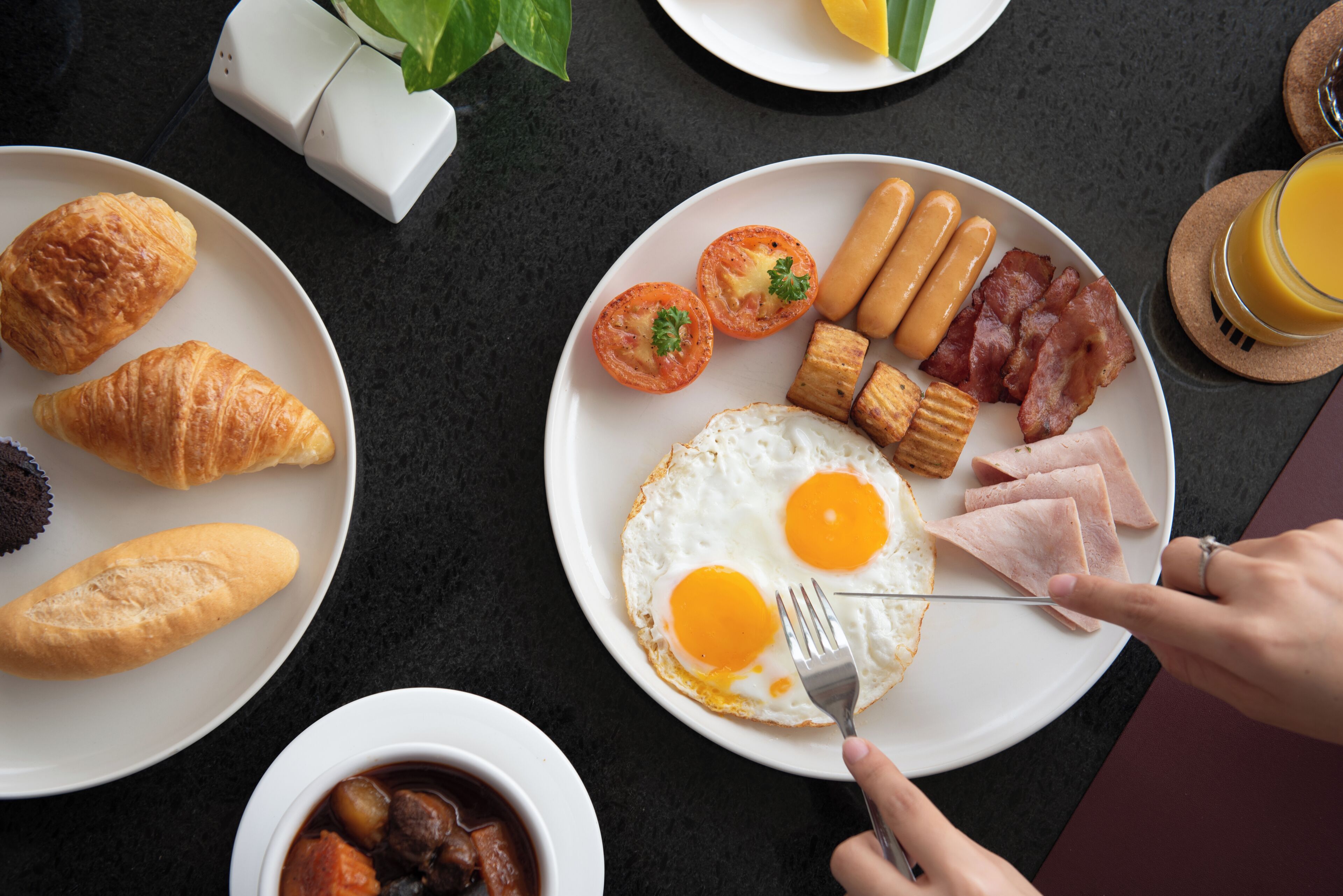 A breakfast spread with croissants, eggs, sausages, bacon, and tomatoes on a table.