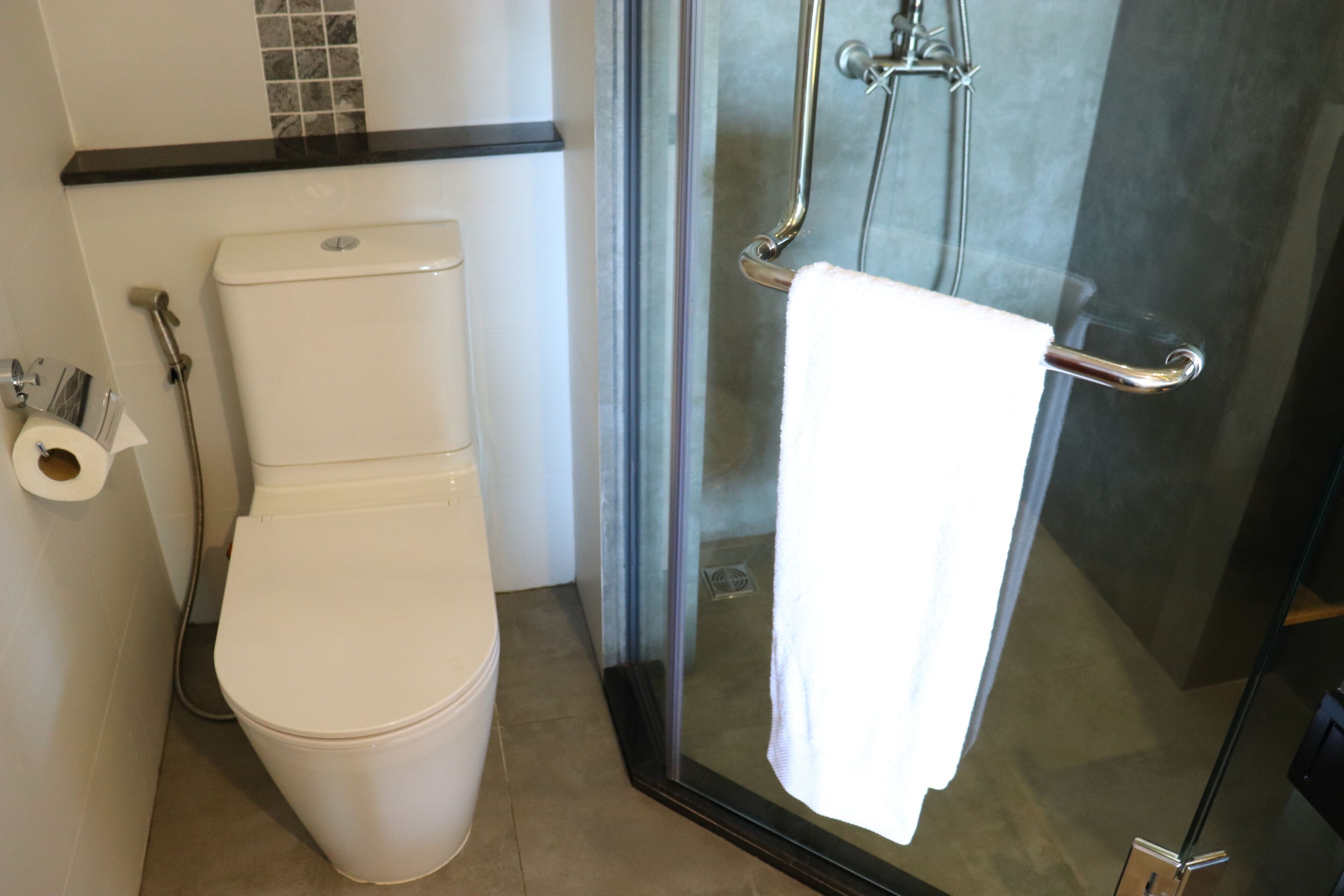 Un baño moderno con cabina de ducha de vidrio, inodoro blanco y toallero.