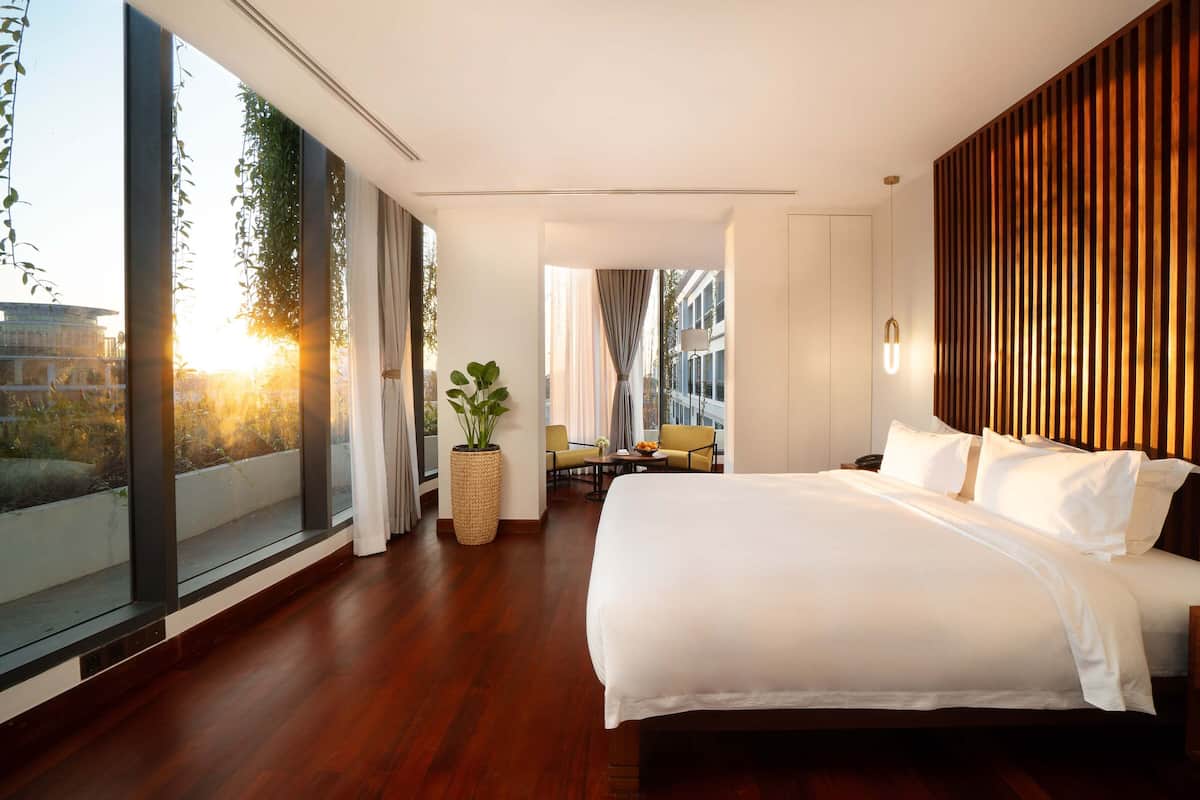 Een moderne hotelkamer met een groot bed, een zithoekje met een tafel en stoelen, en een groot raam met uitzicht over de stad.