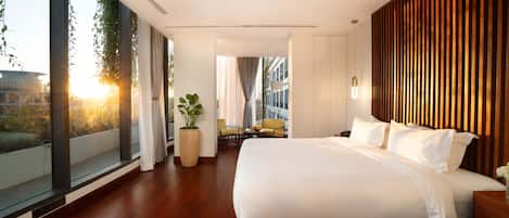 Una habitación de hotel moderna con una cama grande, una pequeña zona de estar con una mesa y sillas, y un ventanal con vistas a la ciudad.