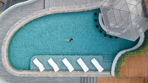 Vue aérienne d’une piscine dotée d’un sol carrelé, d’un plongeoir et d’un espace détente avec des chaises longues blanches.