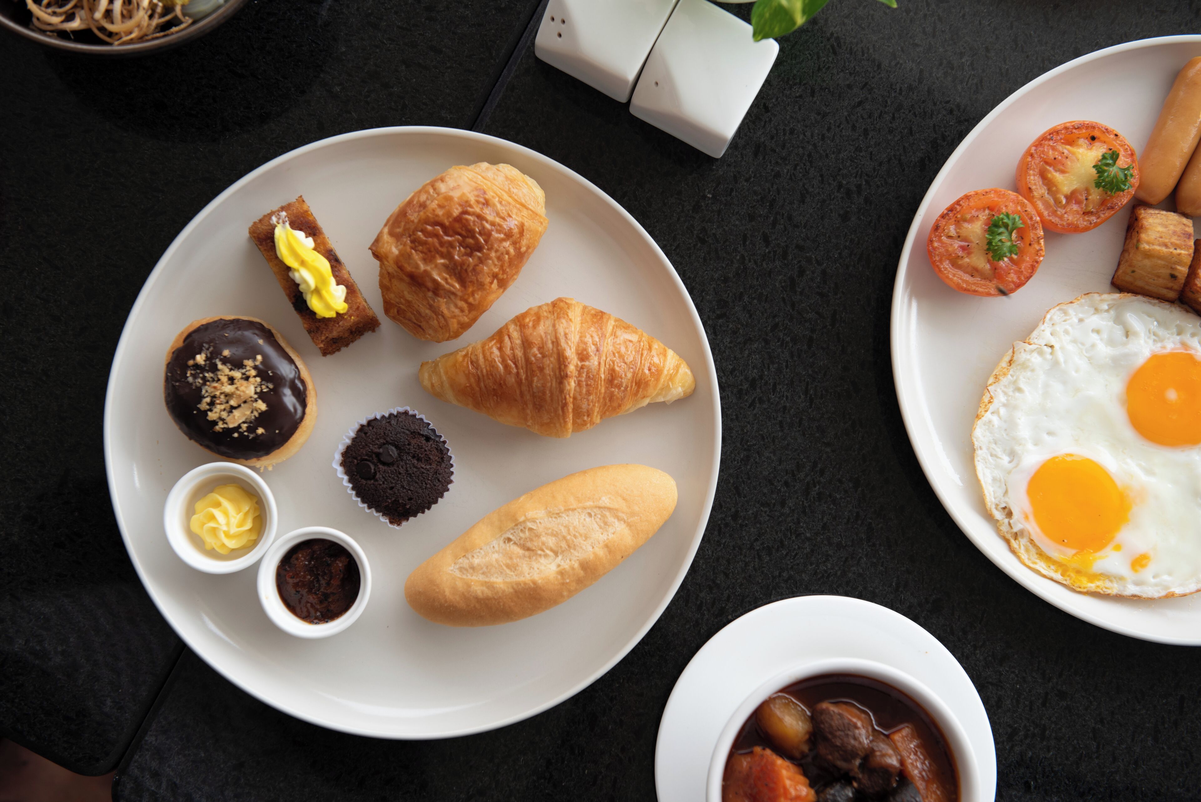 Ein Frühstücksteller mit Croissants, einem Schokoladen-Donut, einem Muffin und einer kleinen Schale Marmelade.