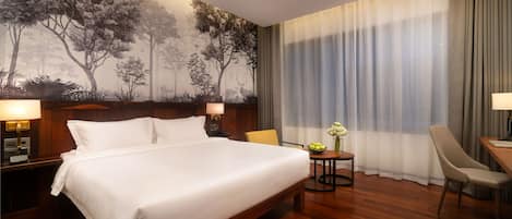 A hotel room with a large bed, a wooden headboard, a nightstand with a lamp, a small table with a vase of flowers, a chair, and a desk with a lamp.