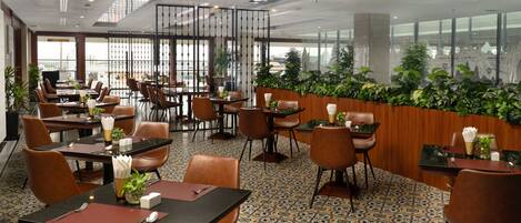 A restaurant with multiple tables and chairs, a patterned floor, and large windows with a city view.