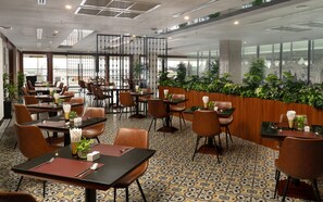 A restaurant with multiple tables and chairs, a patterned floor, and large windows with a city view.