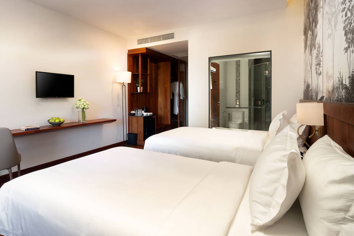 Een hotelkamer met twee bedden, een bureau met stoel, een televisie en een badkamer met douche en toilet.