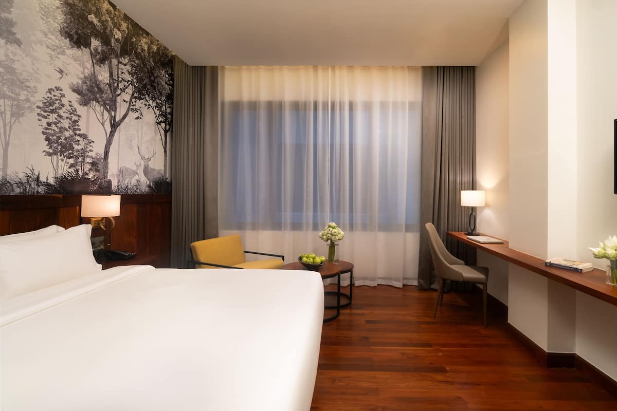 Een hotelkamer met een bed, een bureau met stoel, een kleine tafel met bloemenvaas en een televisie aan de muur.