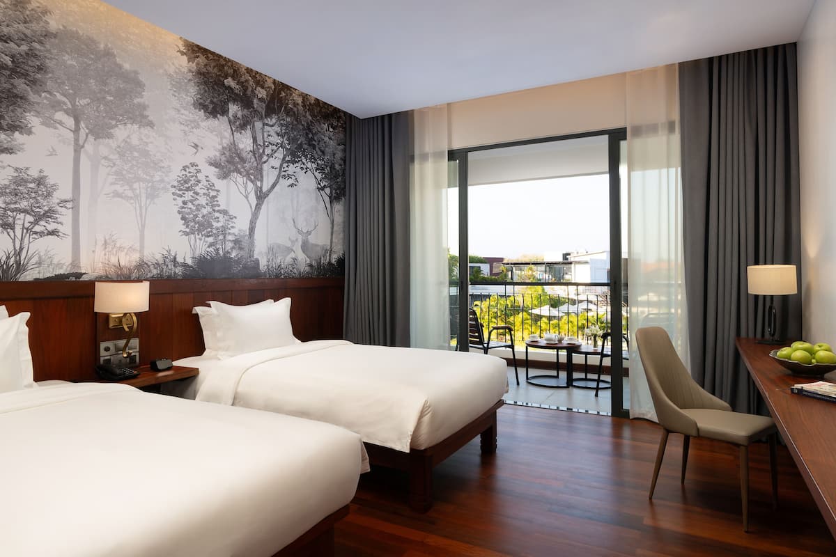 Hotelkamer met twee bedden, een bureau met stoel, een balkon met tafel en stoelen, en een groot muurschildering van een bos.