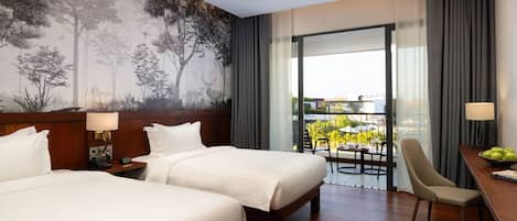 Habitación de hotel con dos camas, un escritorio con silla, un balcón con mesa y sillas, y un mural grande con motivos forestales en la pared.