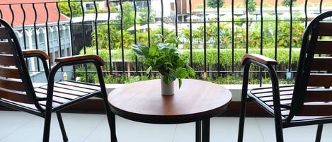 Un balcon avec deux chaises en bois et une petite table, une plante en pot, et une vue sur un jardin et des bâtiments.