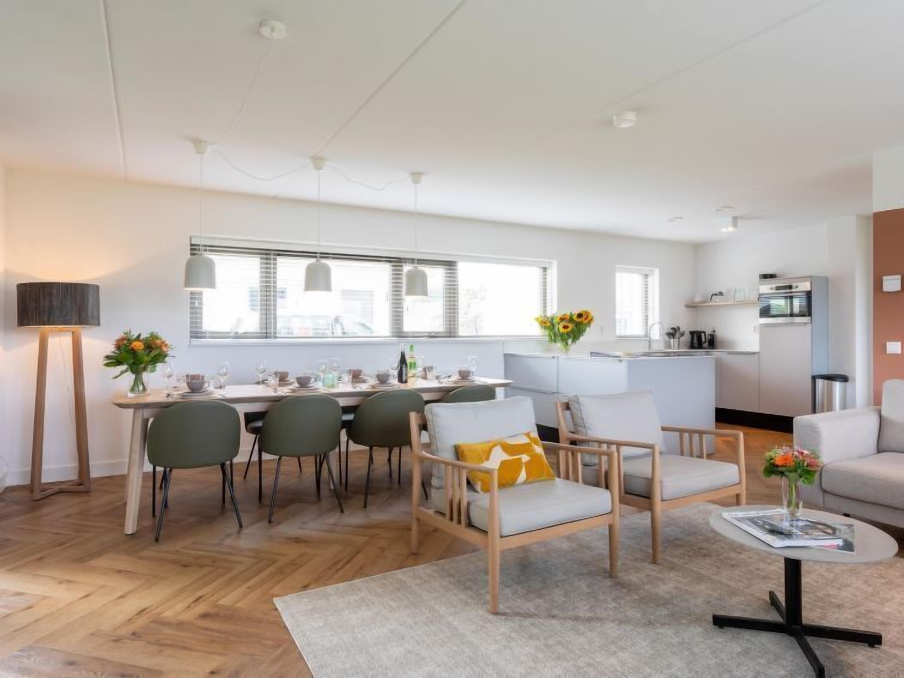 Een moderne woonkamer met een eethoek, keuken en een groot raam dat voor natuurlijk licht zorgt.