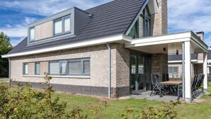 Ett modernt hus i två våningar med ett sluttande tak, stora fönster och en täckt uteplats.