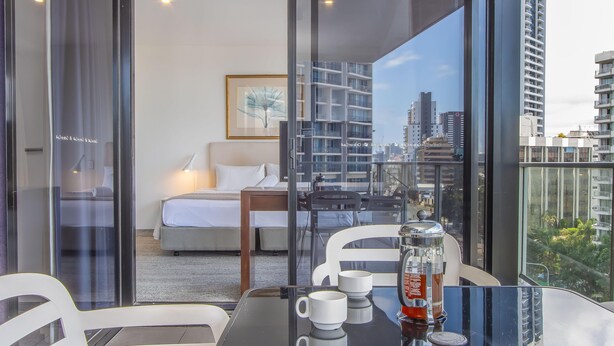 A modern hotel room with a bed, bedside table, and a city view through large windows. - Circle on Cavill - Stunning River Views! (Surfers Paradise)