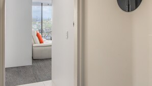 A modern interior with a white wall, a door leading to a room with a white sofa and a city view, and a black circular sign with the number 2067. - Circle on Cavill - Stunning River Views! (Surfers Paradise)
