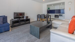 A modern living room with a flat-screen TV, a dark entertainment unit, a blue sofa, a white sofa, and a dining area with a table and chairs. - Circle on Cavill - Stunning River Views! (Surfers Paradise)