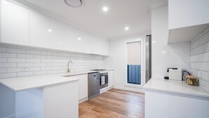 A modern kitchen with white cabinetry, a stainless steel oven, and a wooden floor. - Elegance and Style (Wagga Wagga)