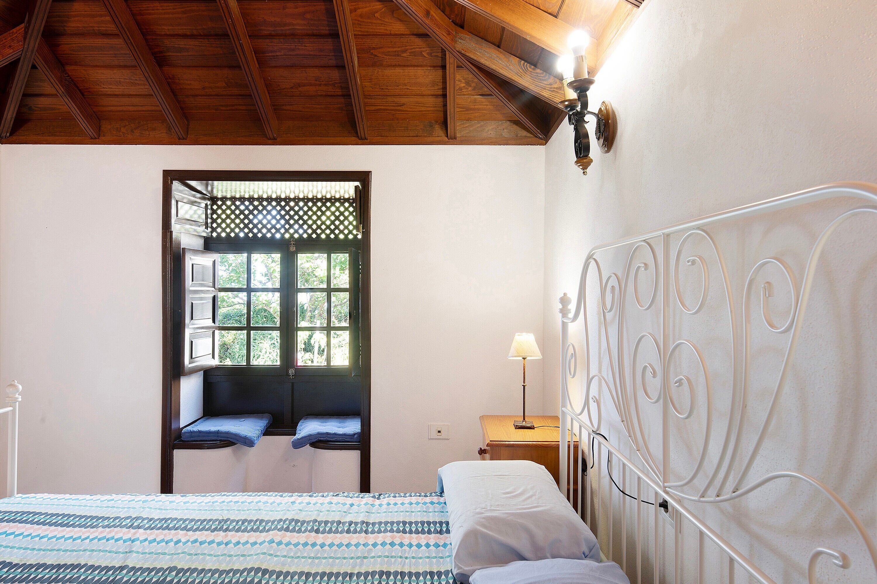 Un dormitorio con cama, ventana con vistas, mesita de noche y lámpara de pared.