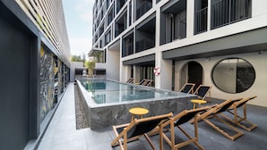 Un espace piscine extérieur moderne, doté d’une piscine rectangulaire, de chaises longues et d’une petite table ronde.