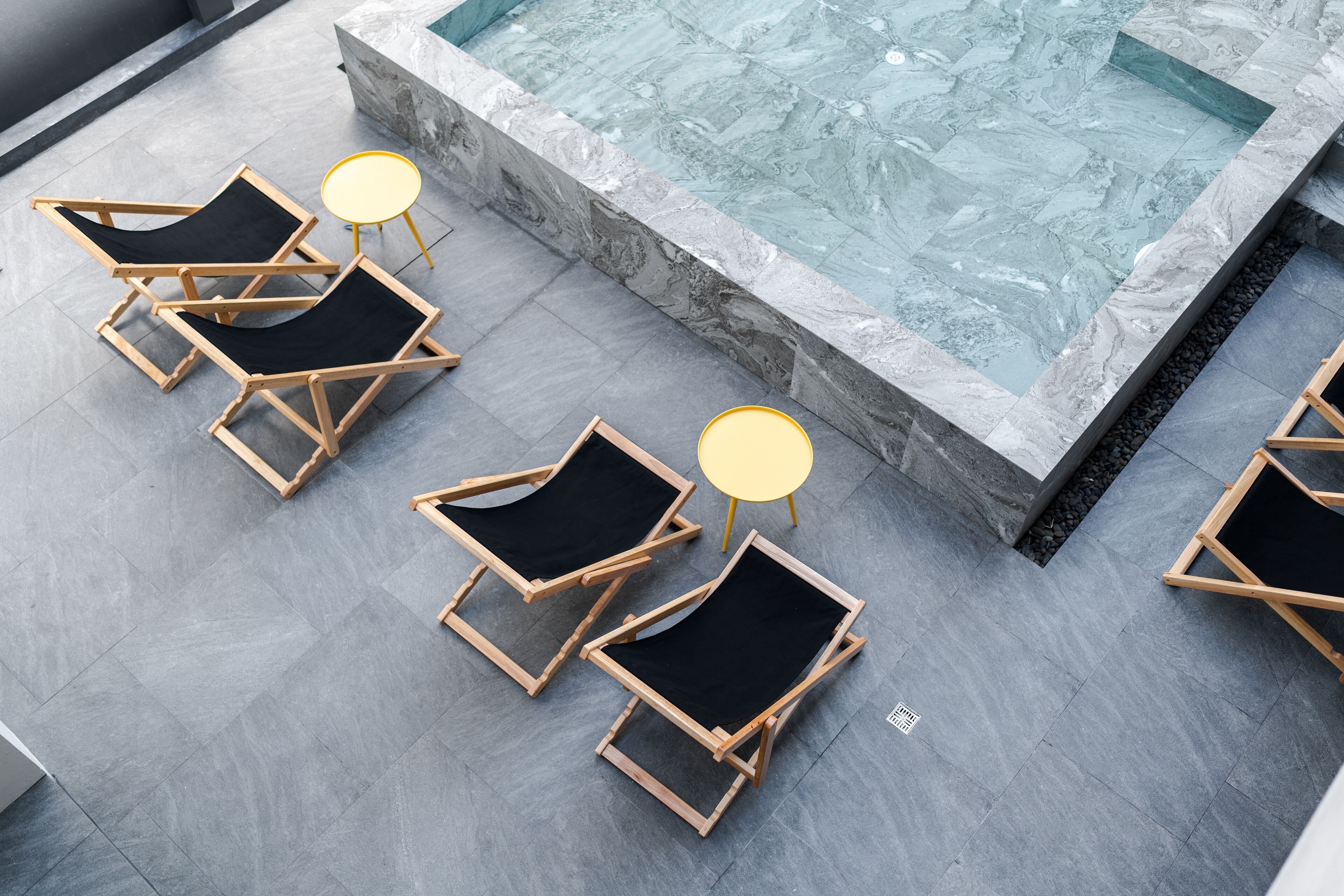 A poolside area with multiple lounge chairs and small round tables, surrounded by a tiled deck.