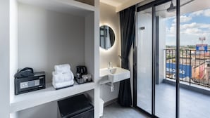 Une salle de bain moderne avec un lavabo blanc, un miroir et une valise noire posée sur une étagère.
