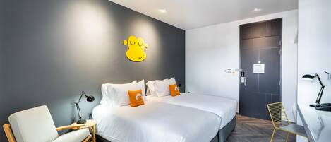 Ein modernes Hotelzimmer mit einem großen Bett, einem Holzstuhl, einem Schreibtisch mit Lampe und einer Wandleuchte.
