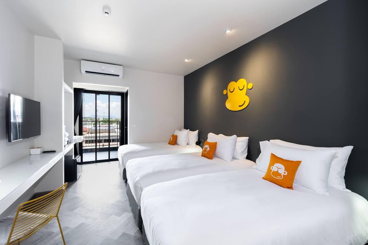 Ein Hotelzimmer mit drei Betten, einem Schreibtisch und einem Fernseher.