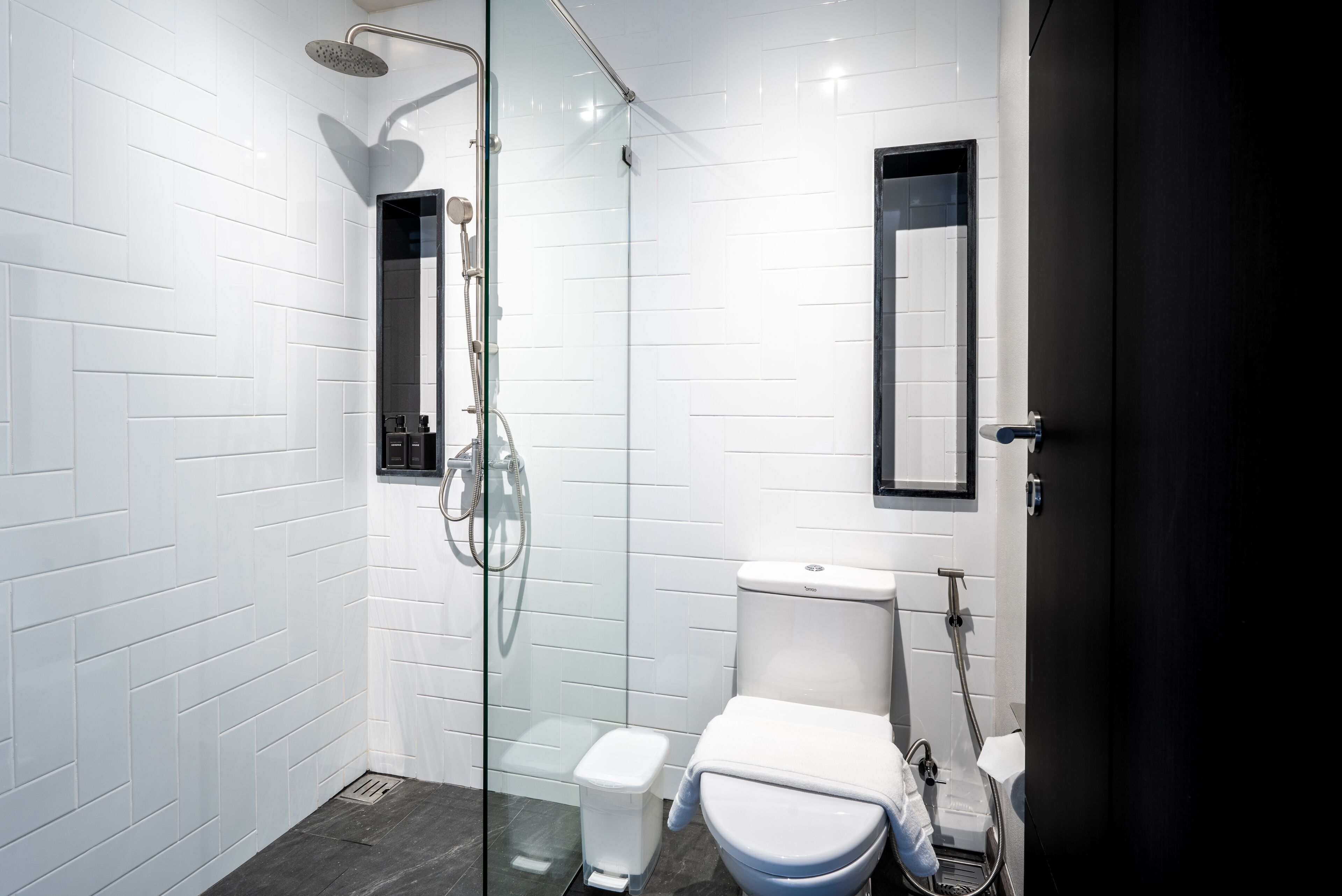A modern bathroom with white subway tiles, a glass-enclosed shower, a toilet, and a black-framed mirror.