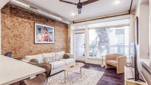 Una sala de estar moderna con pared de ladrillo, ventilador de techo, ventana grande con vista a una escalera y televisor de pantalla plana montado en la pared.