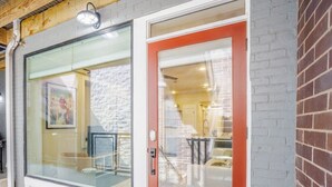 Un edificio con puerta de cristal y puerta roja, terraza de madera y pared de ladrillo.