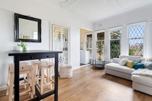 Una sala de estar moderna con una mesa negra, sillas de madera, un sofá blanco y ventanas amplias.