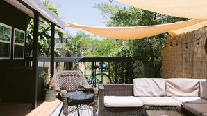 An outdoor patio with a sofa, a chair, and a table. There is a string of lights above and a canopy providing shade.